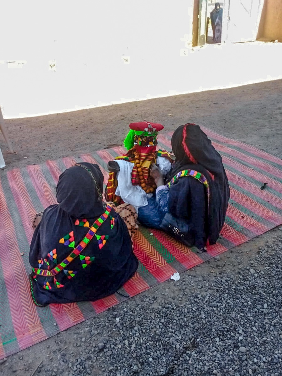 امرأتان جالستان على زربية تُلبسان دمية تلغنجا